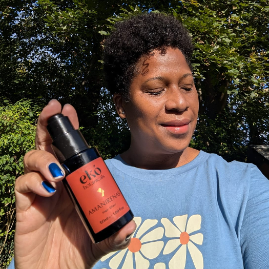 black lady holding a bottle of Hair Growth Oil Elixir AMANIRENAS