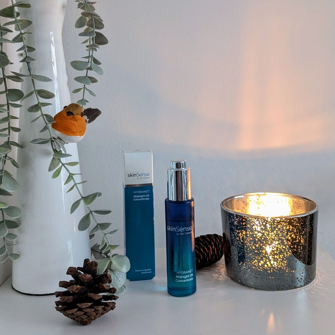 SkinSense Midnight Oil Concentrate candles greenery and robin in the backdrop
