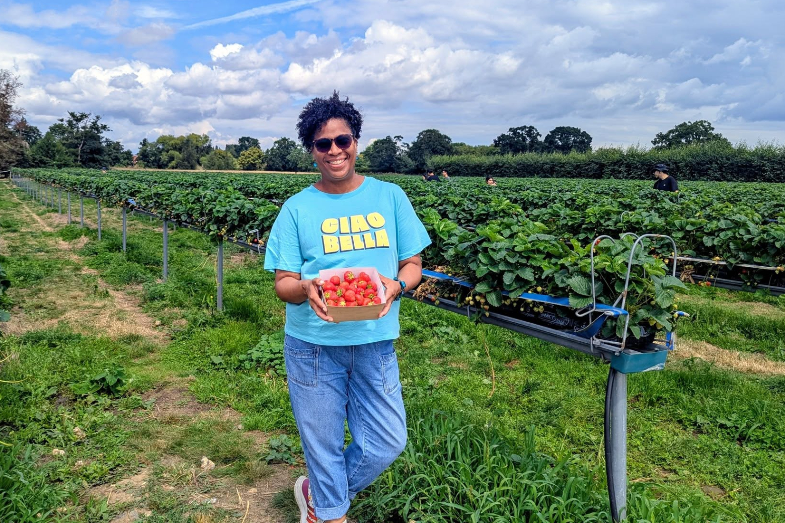 black woman in a strawberry field holding box of strawberries