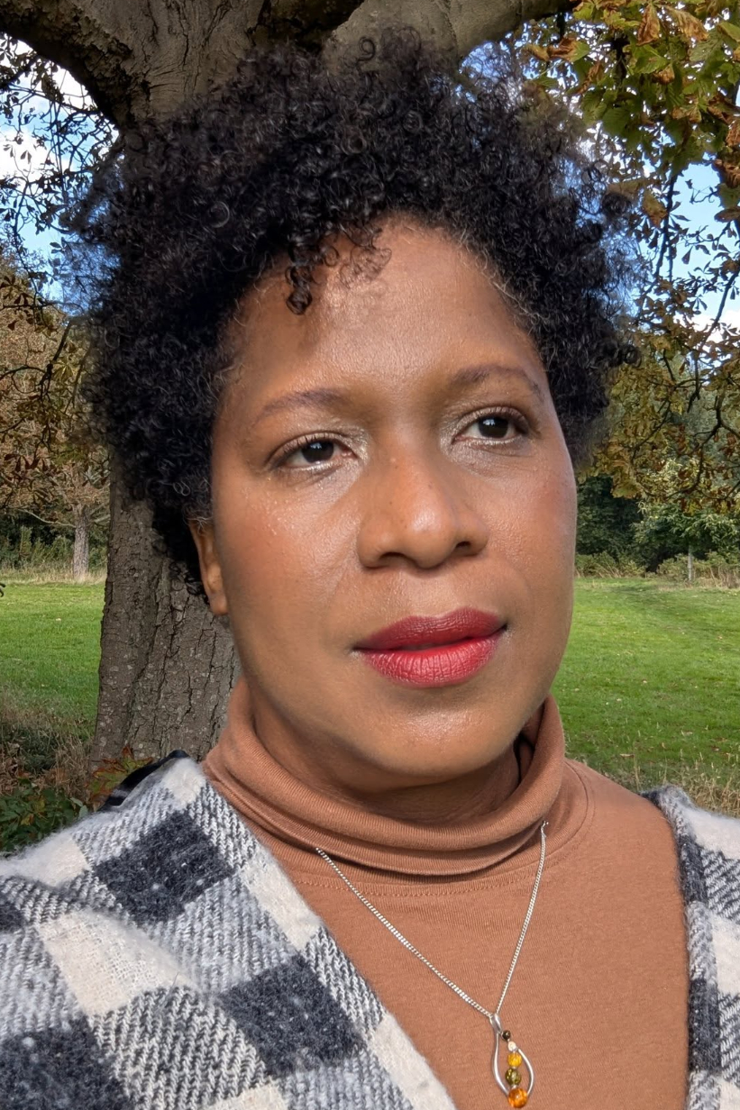 black women wearing bold red lipstick nuetral eyeshaow standing in front of a tree on a bright sunny day.