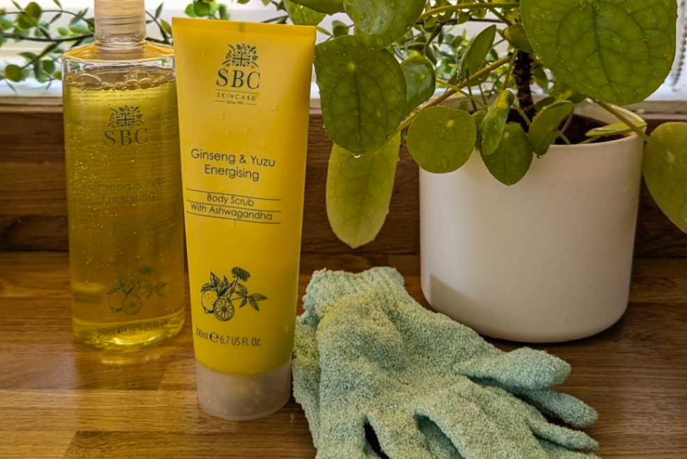 Ginseng & Yuzu shower collection next to a money plant on a wooden countertop with a yellow blend in the background