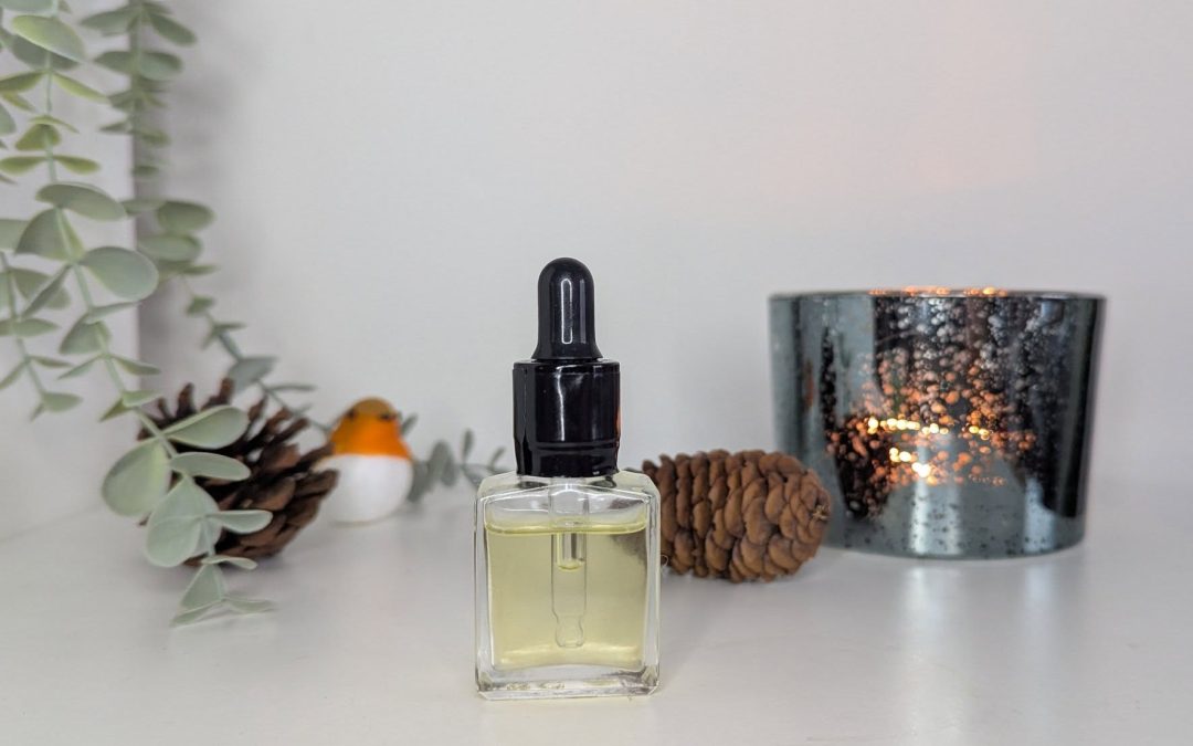 small bottler of oil with pine cones and candles in the backdrop